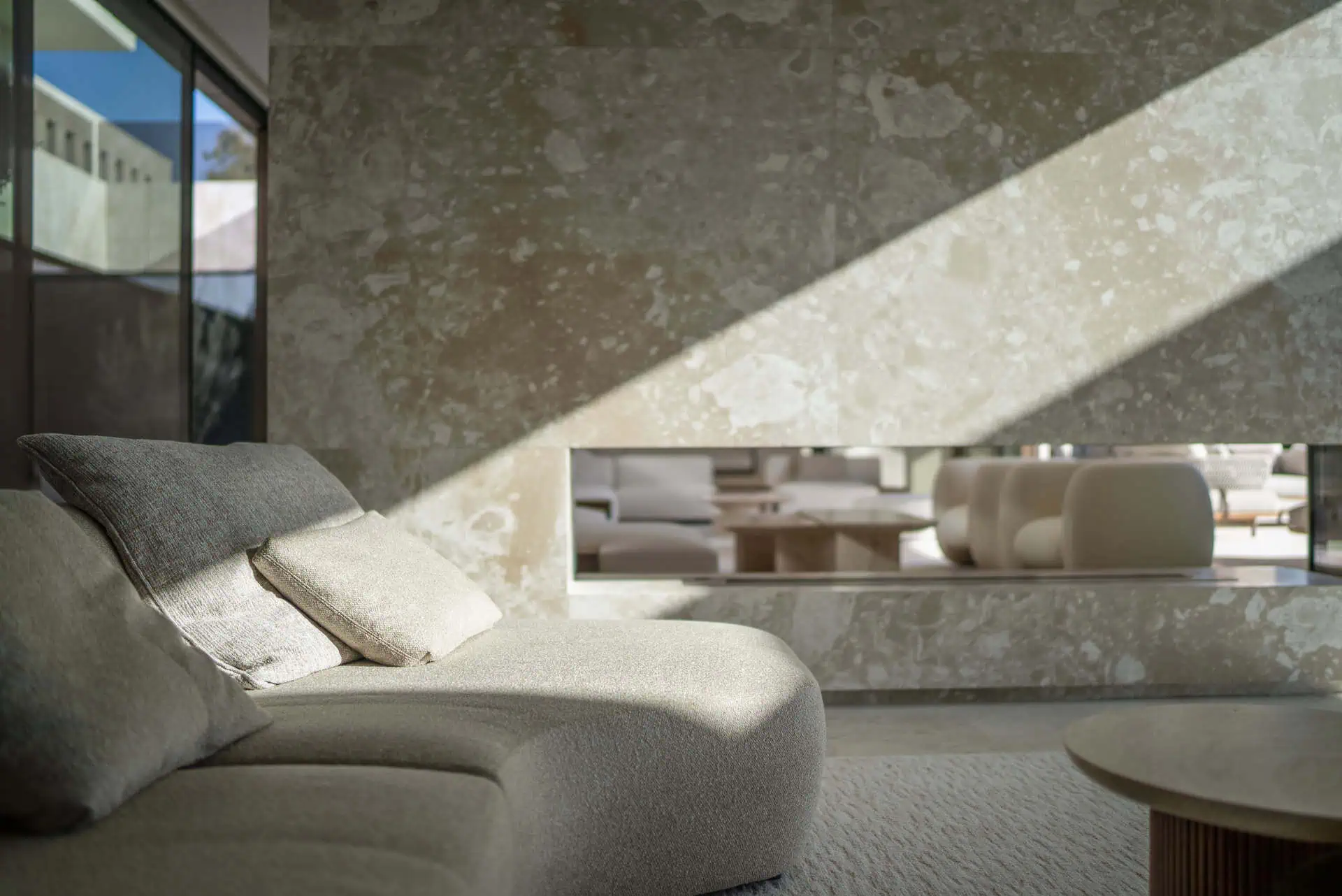 modern living room with natural light streaming across a textured travertine wall, illustrating how material and light create emotion and atmosphere in ARK Architects’ design philosophy