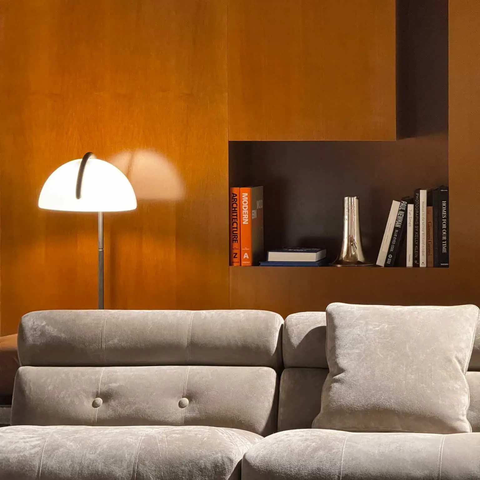 elegant modern living room with a plush light-gray sofa, designer floor lamp, and built-in wooden shelving displaying books and decorative objects