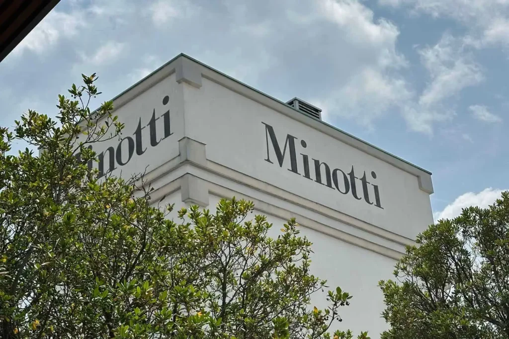 exterior view of the minotti headquarters in Meda, Milan, featuring the iconic Minotti logo on a white building surrounded by greenery.