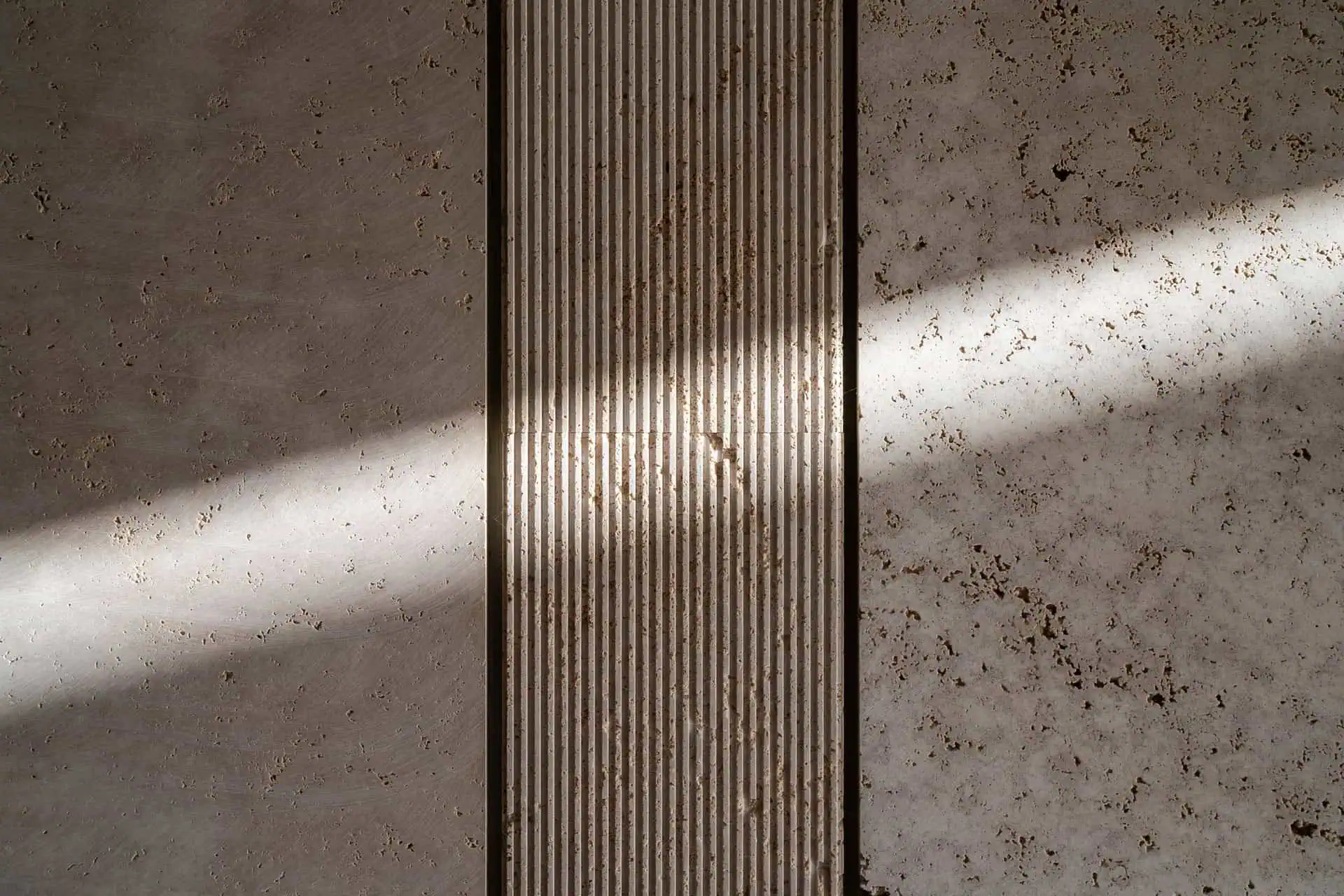 detail of sandblasted travertine wall showing how light interacts with different textures, highlighting the material’s unique response and creating a sensory atmosphere, as conceived by ARK Architects and Manuel Ruiz Moriche