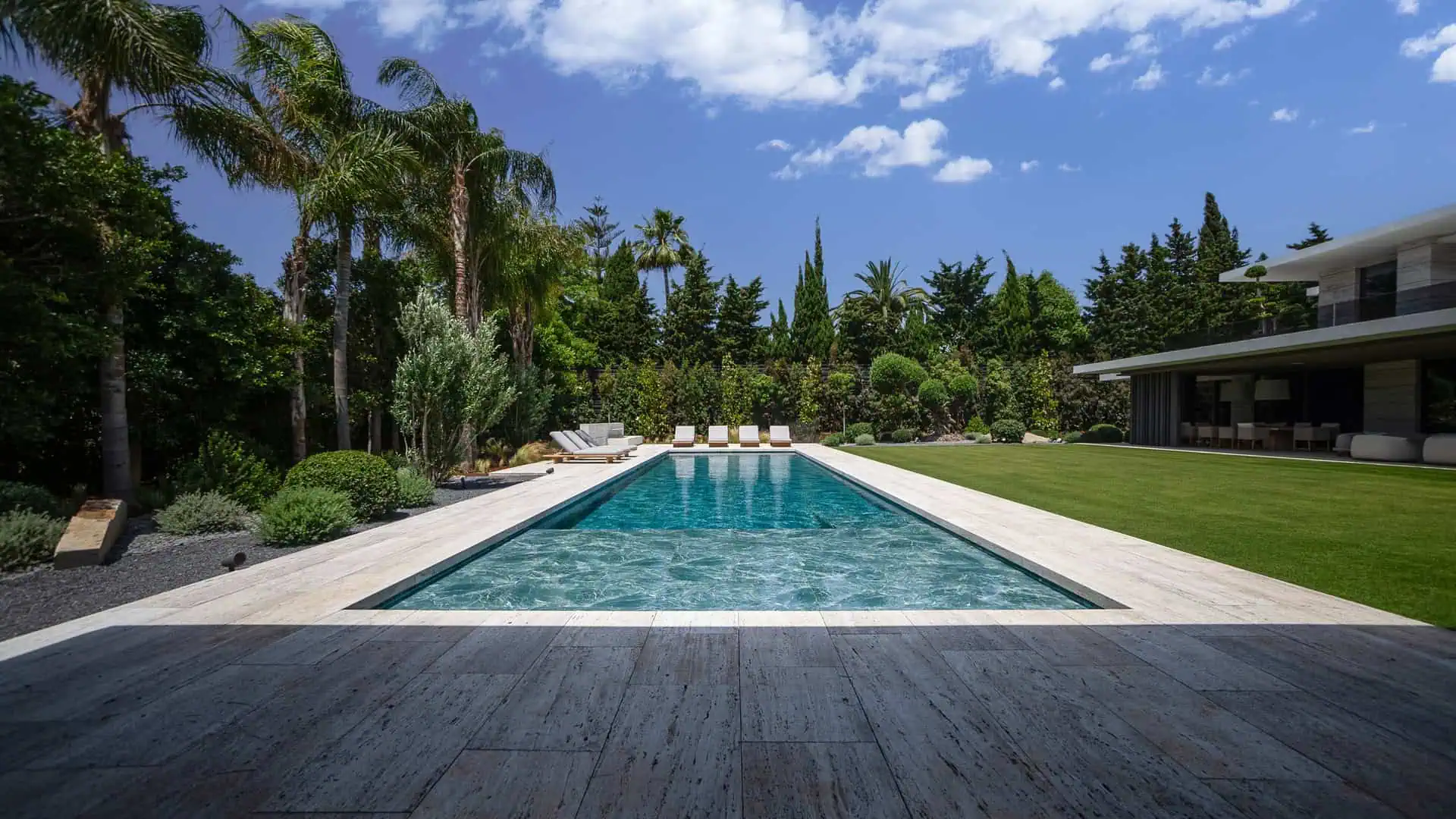 Modern pool surrounded by lush Mediterranean landscaping and palm trees at Villa TIERRA by ARK Architects in Sotogrande