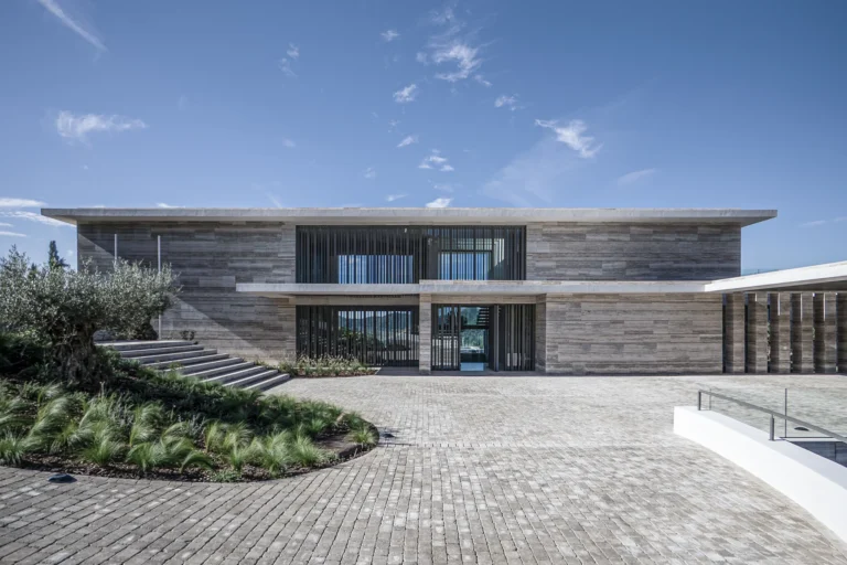 Exterior facade of Villa Geneve by ARK Architects, showcasing modern travertine stone architecture and Mediterranean landscaping